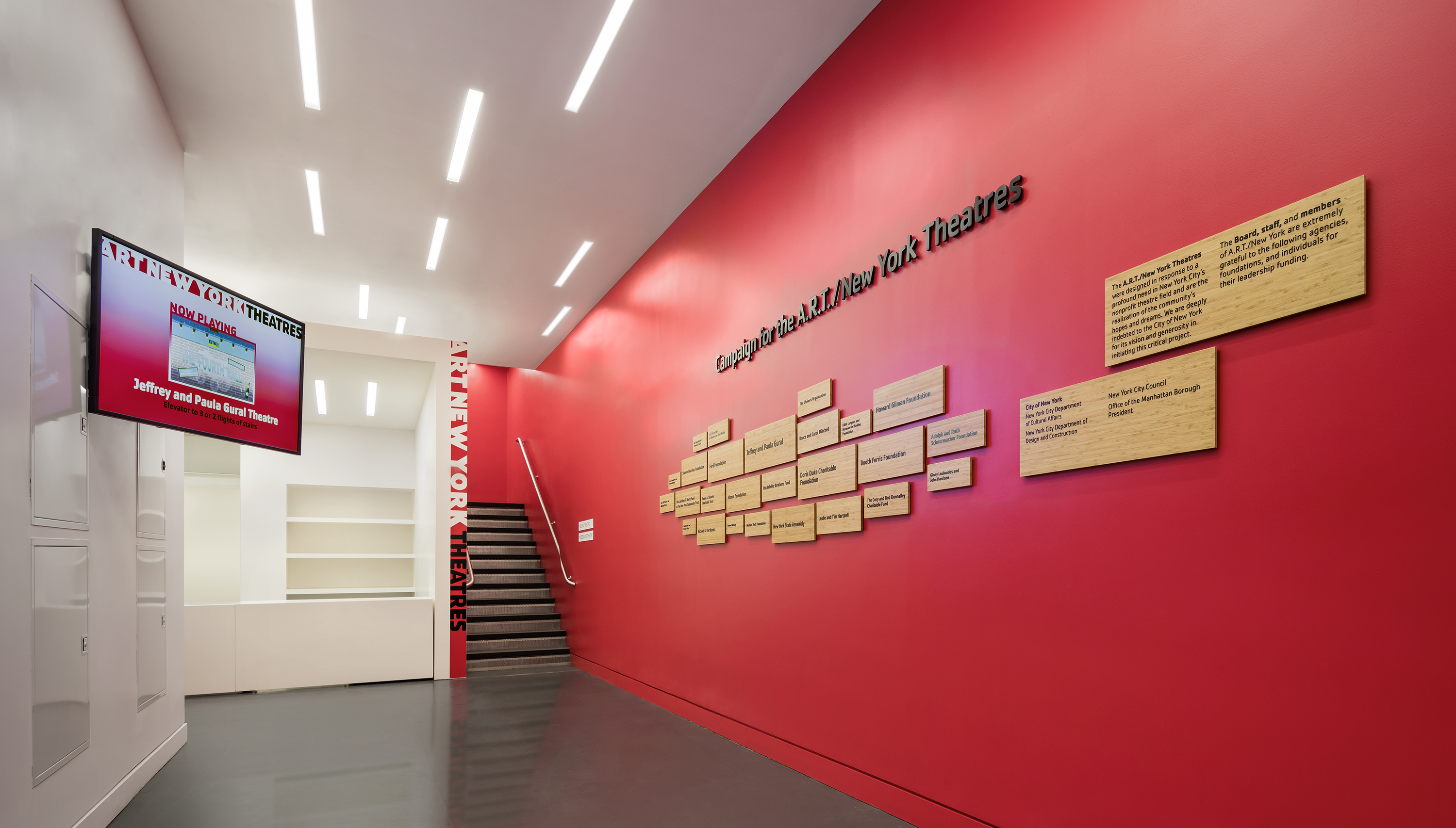 The lobby of the ART/NY Theatres. A monitor displays information about a show. The righthand wall has several plaques listing prominent donors.